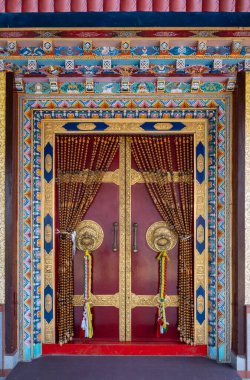 Bylakuppe, Mysore Bölgesi, Karnataka, Hindistan 'daki Namdroling Budist Manastırı' ndan Padmasambhava Vihara 'nın giriş kapısının etrafındaki dekore edilmiş kırmızı şarap çerçevesi.