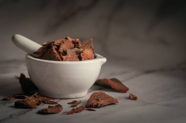 Beyaz seramik havan ve tokmak içinde Dry Arjuna Barks (terminalia arjuna) kabukları yakın çekim. Marbel arkaplanda ön görünüm.