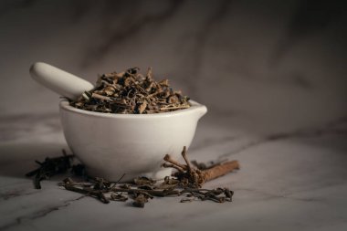 Kuru Punarnava (Boerhaavia diusa) kökleri ve yaprakları, beyaz seramik havan ve tokmak. Marbel arkaplanda ön görünüm.