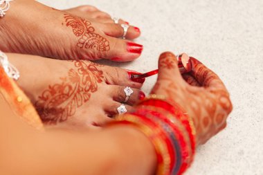 Beautiful Indian bride applying red nail polish on her nails carefully. clipart