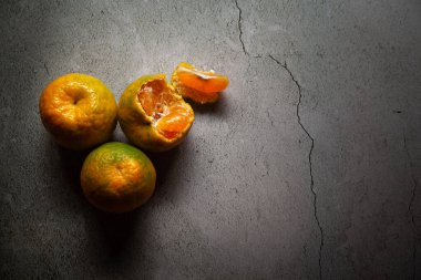 Hint organik portakallarının üst görüntüsü ve mermer bir masanın üzerinde soyulmuş bir portakal (Citrus sinensis). Karanlık ve kasvetli sahne.