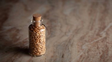 Organik buğdayla dolu küçük bir cam şişe (Triticum) mermer bir zemin üzerine yerleştirilir..