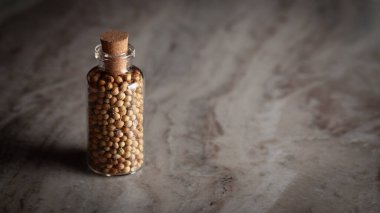 Kurumuş organik kişniş (Coriandrum sativum) tohumlarıyla dolu küçük bir cam şişe mermer arka plana yerleştirilir..