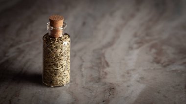 A small glass bottle filled with organic Fennel Seeds (Foeniculum vulgare) Badi saunf is placed on a marble background. clipart