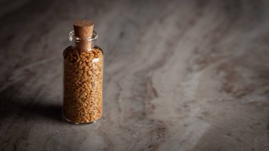 Organik FenuGreek tohumu (Trigonella foenum-graecum) ile dolu küçük bir cam şişe mermer zemin üzerine yerleştirilir..