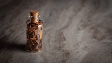 Organik tarçın (Cinnamomum verum) veya dalchini ile dolu küçük bir cam şişe mermer bir arka plan üzerine yerleştirilir..