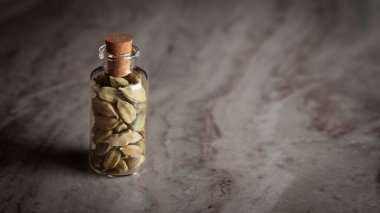 A small glass bottle filled with organic Cardamom or cardamum (Elettaria cardamomum) is placed on a marble background. clipart