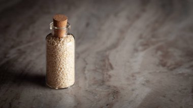 Organik Beyaz Susam tohumu (Sesamum indicum) veya Til ile dolu küçük bir cam şişe mermer zemin üzerine yerleştirilir.
