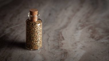 Kurumuş Oregano yapraklarıyla dolu küçük bir cam şişe mermer bir arka plana yerleştirilmiş..
