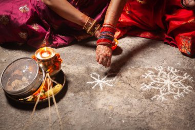 Two Indian women are making an Auspicious Hindu design pattern (rangoli) for the Karwa Chauth Festival. clipart