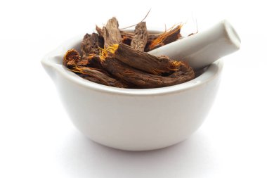 Beyaz bir zemin üzerinde izole edilmiş beyaz seramik havan ve tokmak, kuru organik Sugandh Mantri (Homalomena aromatica) yakın plan.
