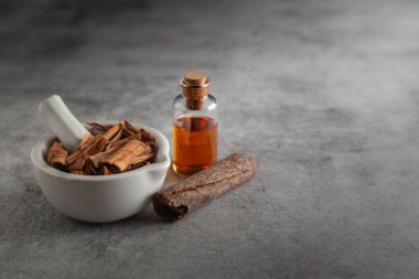 Kuru organik tarçın çubukları (Tarçın verum), beyaz seramik havan ve tokmak, temel yağ ile birlikte.