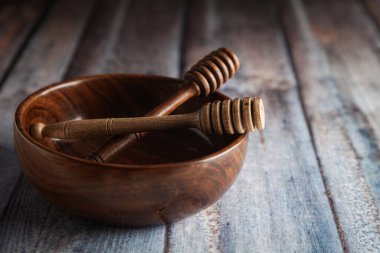 Tahta bir kase, ahşap bir bal damlatıcısıyla birlikte ahşap bir arka plana yerleştirilir..