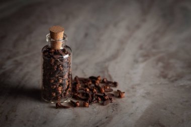 Organik karanfil (Syzygium aromaticum) ya da Hint aromaticum ile dolu küçük bir cam şişe mermer zemin üzerine yerleştirilir..