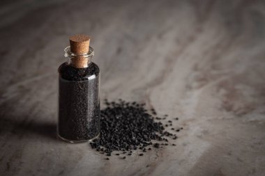 Organik siyah kimyon (Nigella sativa) veya kalonji ile dolu küçük bir cam şişe mermer zemin üzerine yerleştirilir..