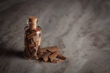 Organik tarçın (Cinnamomum verum) veya dalchini ile dolu küçük bir cam şişe mermer bir arka plan üzerine yerleştirilir..