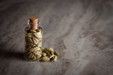 Organik kakule veya kardamum (Elettaria cardamomum) ile dolu küçük bir cam şişe mermer zemin üzerine yerleştirilir..