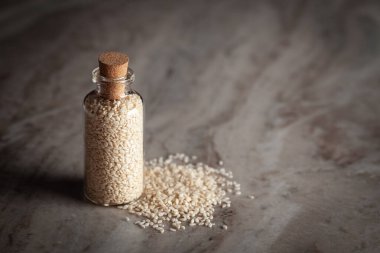 Organik Beyaz Susam tohumu (Sesamum indicum) veya Til ile dolu küçük bir cam şişe mermer zemin üzerine yerleştirilir.