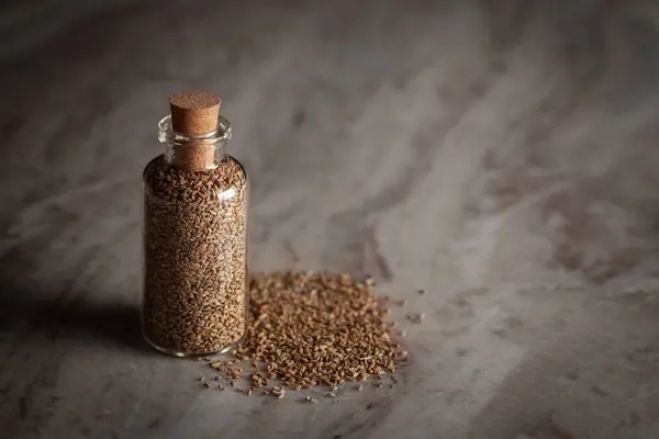 stock image A small glass bottle filled with organic Carom seeds (Trachyspermum ammi) or Ajwain is placed on a marble background.