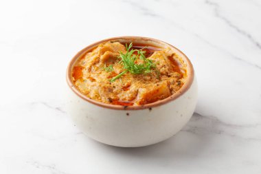 Paneer Tereyağlı Masala ya da Peynirli Köfte Körisi tabakta servis edilen taze yeşil kişniş yapraklarıyla süslenmiş, beyaz granit arka planda seramik bir kasede servis edilir Seçici odak noktası