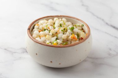 Sabudana Khichadi 'nin yakın çekimi - Maharashtra' dan sago tohumlarıyla yapılmış ve seramik kasede servis edilen kişniş yapraklarıyla süslenmiş otantik bir yemek