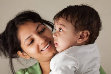 Hintli mutlu anne ve bebek gri arka planda başkalarına bakıyor.