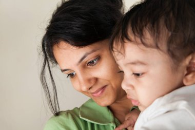 Hintli mutlu anne ve bebek gri arka planda başkalarına bakıyor.