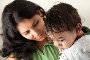 Hintli mutlu anne ve bebek gri arka planda başkalarına bakıyor.