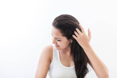 20 'li yaşlarda güzel bir Hintli kadın beyaz bir bluz giyiyor, saçını düzeltiyor, beyaz bir arka planda..