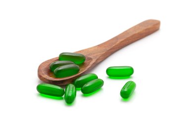 Sağlık hizmeti konsepti. E vitamini (Yeşil) tıbbi kapsüllerle dolu tahta bir kaşık. Beyaz bir arkaplanda izole edilmiş.