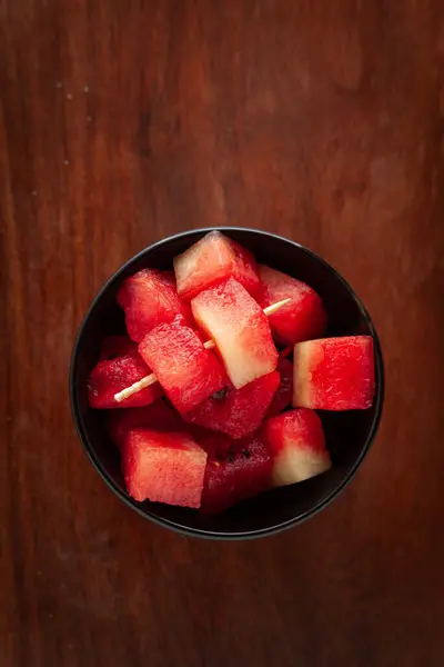 stock image A black ceramic bowl filled with Organic watermelon (citrullus Lanatus) cubes, on a wooden table.