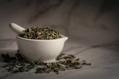 Kuru Organik Jimnastik veya Gurmar (Gymnema sylvestre) yapraklarının beyaz seramik havan ve tokmak, mermer bir zemin üzerinde yakın plan.