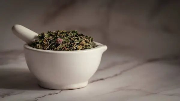 stock image Close-up of Dry Organic Gymnema or Gurmar (Gymnema sylvestre) leaves, in white ceramic mortar and pestle, on a marble background.