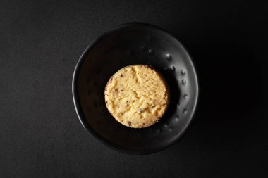 Siyah arka planda siyah bir kaseye yerleştirilmiş tam buğday parçacıklı kurabiye..