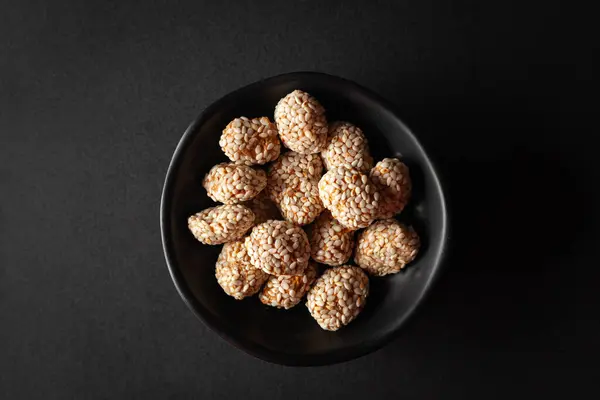 stock image Top view of a black bowl filled with Indian sweet item called 'Rewri' or 'Revdi' or Sesame seeds sweet, on a black background.