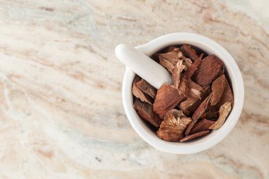 Kuru Organik Arjuna (Terminalia Arjuna) kabukları, beyaz seramik havan ve tokmak, mermer zemin üzerinde.