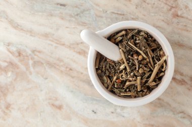 Kuru Organik Ashwagandha (Withania somnifera) yaprakları beyaz seramik havan ve tokmak, mermer bir zemin üzerinde.