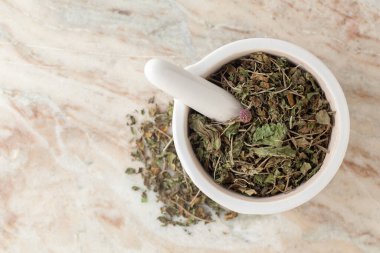 Kuru Organik Jimnastik veya Gurmar (Gymnema sylvestre) yaprakları beyaz seramik havan ve tokmak, mermer zemin üzerinde.
