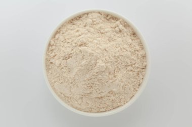 Beyaz seramik bir kasede organik buğday unu (Triticum) bulunur. Gri bir arka planda izole edilmiş. Üst Görünüm