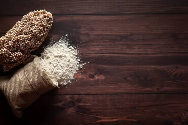 Stock image Organic Sorghum Flour (Sorghum bicolor) spilled out from a jute bag with seeds, isolated on a dark wooden background. Top view.