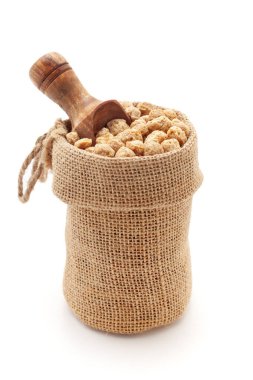 Organik Soya Parçalarının (Glycine max) yakın plan çekimi, beyaz bir arkaplanda izole edilmiş bir kepçeyle bir jüt torba içinde.