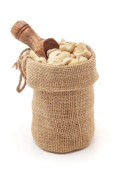 stock image Close-up of organic Cashew nuts (Anacardium occidentale) in a jute bag with a scoop, isolated on a white background.