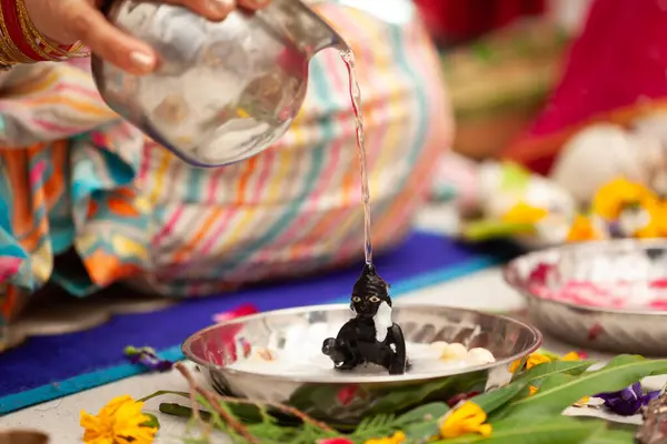 stock image Indian woman performing snan ritual by pouring water on (Laddu Gopal) Hindu god Krishna, during the Indian festival of Krishna Janmashtami.