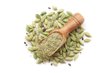 Organik kakule (Elettaria kakule) tozu ile dolu ahşap bir kepçe, beyaz bir arka planda izole bir kakule yığını üzerine yerleştirilir..