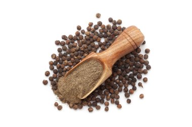 Karabiber (Piper nigrum) tozuyla dolu ahşap bir kepçe, beyaz bir arka planda izole edilmiş, bir yığın siyah biberin üzerine yerleştirilmiş..