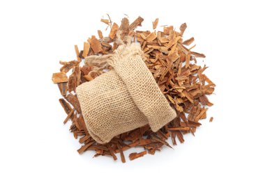 Tarçın çubuklarının (Cinnamon verum) beyaz bir arka planda izole edilmiş tarçın çubukları yığınının üzerinde bir jüt torba içinde yakın plan görüntüsü.