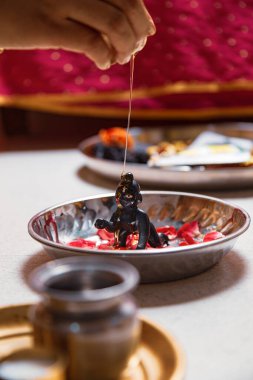 Indian woman performing snan ritual by pouring 'Honey' on (Laddu Gopal) Hindu god Krishna, during the Indian festival of Krishna Janmashtami. clipart