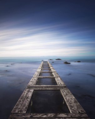 Ahşap iskele ya da güneş doğarken mavi bir denizde iskele. Livorno, Toskana bölgesi. Uzun pozlama fotoğrafı.