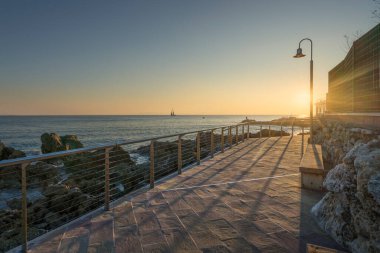 The seafront promenade of Castiglioncello at sunset and a boat in the sea. Province of Livorno, Tuscany region, Italy clipart