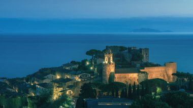 Blue hour over Castiglione della Pescaia, illuminated old town, sea and Giglio Island in the background. Maremma, Tuscany region, Italy, Europe clipart